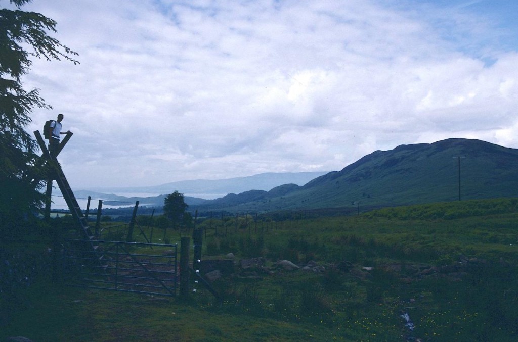 Gavan climbs a stile as views of Loch Lomond, left, and Conic Hill